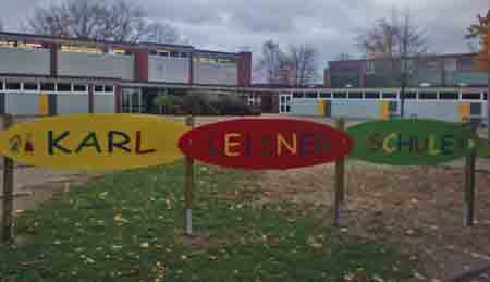 Blick auf ein buntes Schild mit der Aufschrift ´Karl-Leisner-Schule´, im Hintergrund das Schulgebäude